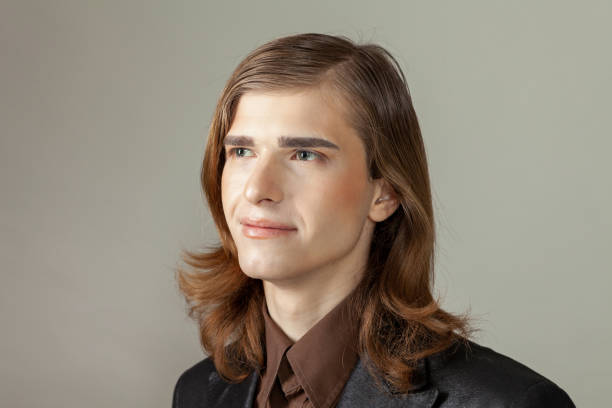 Close-up studio portrait of a non-binary person with long brown hair with make-up in a black jacket on a beige background