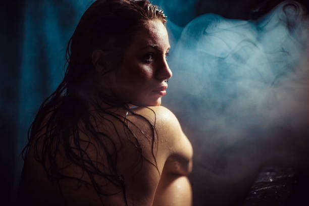 Woman with wet body sitting in dark steamy bathroom stock photo