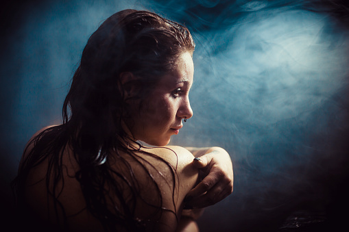 Woman with a wet body sitting in a dark steamy bathroom