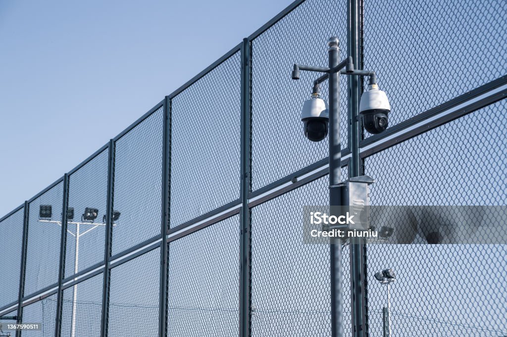 Modern surveillance video cameras, metal mesh and lighting Prison Stock Photo