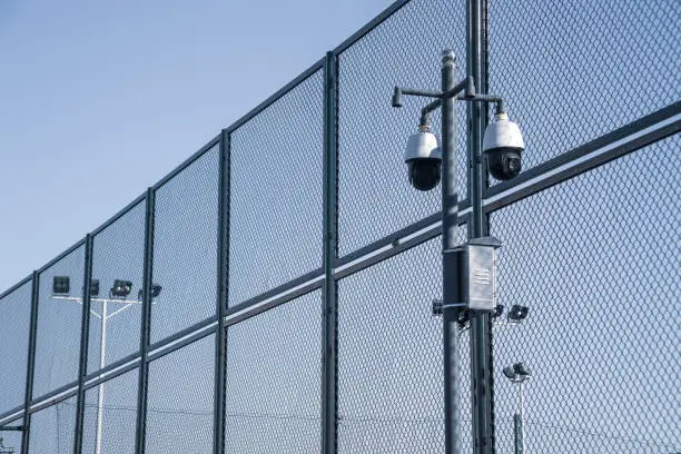 Photo of Modern surveillance video cameras, metal mesh and lighting