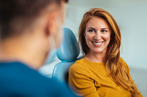 Smiling red haired woman listening to her dentist while sitting in his office