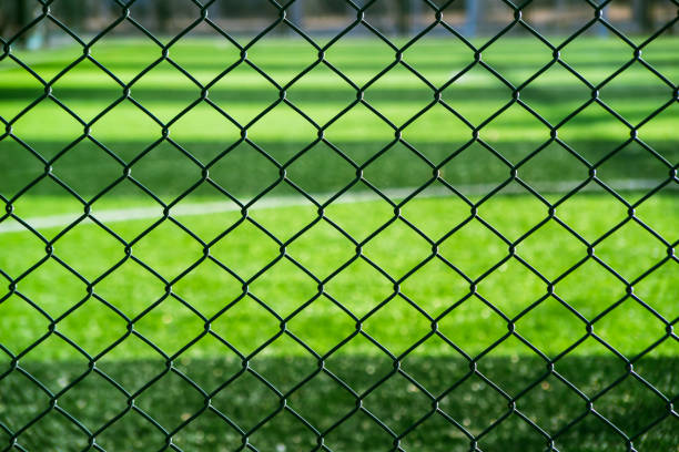 maille métallique et champ d’herbe. arrière-plan du terrain de sport en plein air. - green fence chainlink fence wall photos et images de collection