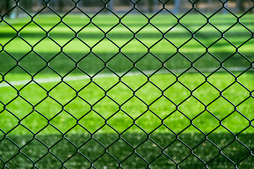 Metal mesh and grass field. Outdoor sports field background.