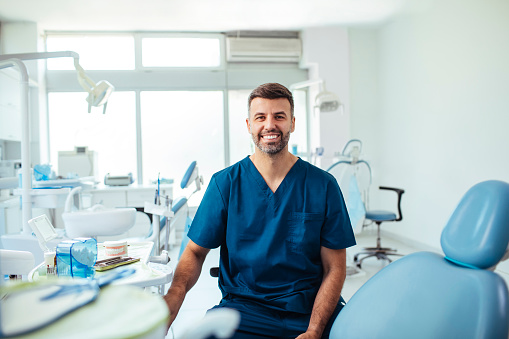 Portrait shot of a young smiling dentist sitting in his clinic