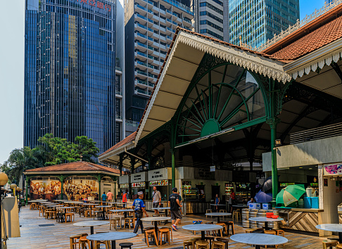 Singapore - September 07, 2019: Customers walking into the street hawker center Lau Pa Sat Telok Ayer Market, downtown skyscrapers in the background