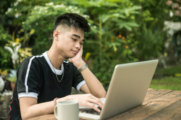 młody mężczyzna z azji południowo-wschodniej jest lekko znudzony lub senny podczas pracy na laptopie w domu lub w parku. - southeast asian ethnicity men laptop image type zdjęcia i obrazy z banku zdjęć