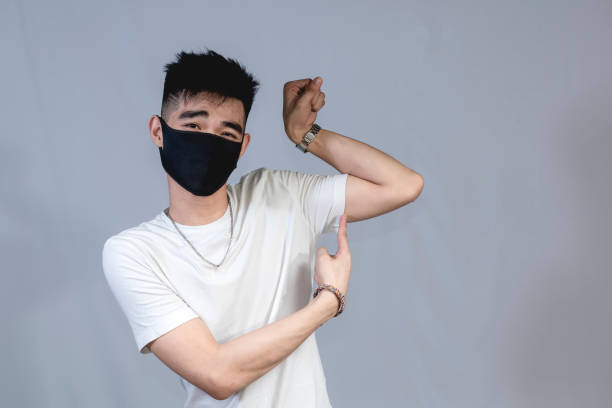 istock A funny young asian male in a black face mask comically flexes his bicep and points at it with his right index finger while playfully looking at the camera. 1367616219
