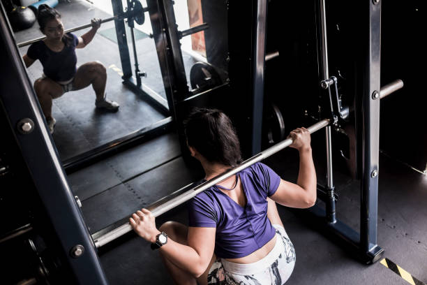 istock An athletic asian girl does some full squats on a smith machine. Working out and training at the gym or fitness club. 1367618944