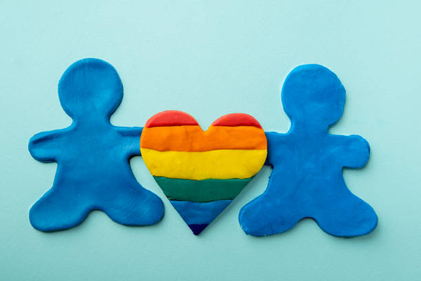 dos hombres idénticos de plastilina azul sostienen una forma de corazón de arco iris de plastilina sobre un fondo azul. concepto de familia lgbt. - childs play clay small men team fotografías e imágenes de stock