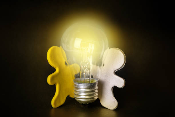 istock Two plasticine men holding a lit light bulb on a black background. Teamwork concept. Creative new idea. 1367623758