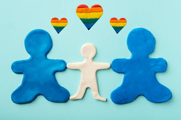 dos hombres idénticos a la plastilina azul que los mismos padres sostienen a un niño de plastilina blanca sobre un fondo azul con corazones de arco iris - childs play clay small men team fotografías e imágenes de stock