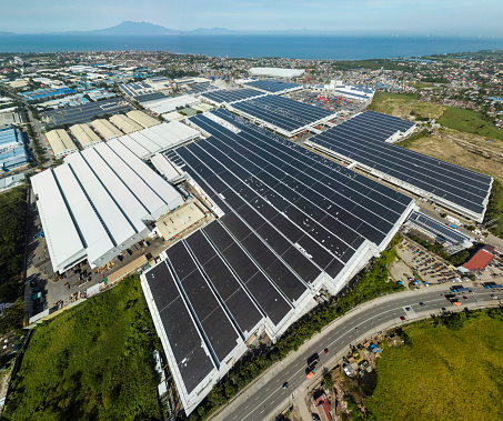 Wide aerial view of a massive building in Cavite Export Processing Zone in Rosario, Cavite, Philippines. The roof is installed with solar panels. Manila bay visible in background.