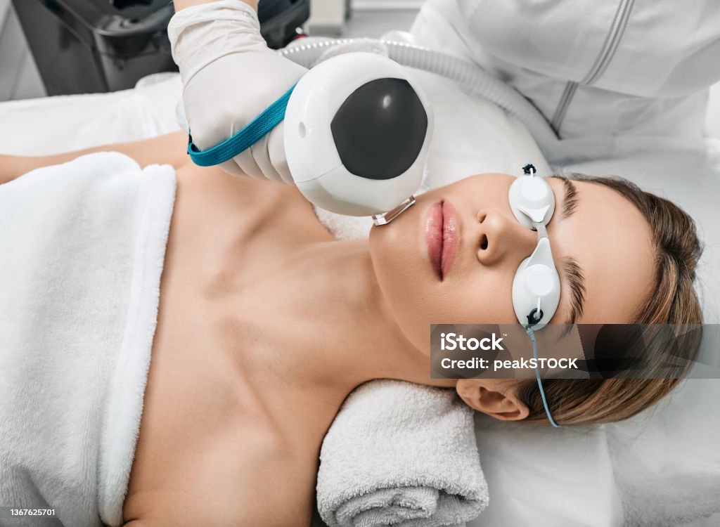 Photorejuvenation of a woman's face using intense pulsed light IPL with a beautician in a cosmetology salon for rosacea treatment, removing brown spots and vascular mesh Facial Mask - Beauty Product Stock Photo