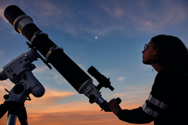 istock Girl with astronomical telescope stargazing under twilight sky. 1367625737