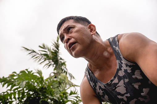 A fit and determined 50 year old asian man in a tank top and an intense ruthless look during a workout. Looking forward while exercising