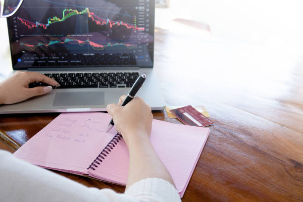 istock Using a computer to view stock market graphs and write them down in a paper notebook makes financial plans on a wooden table. 1367630091