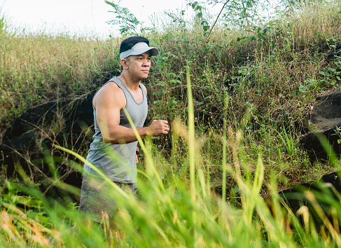 A fit asian runner doing Fartlek Interval Training off the beaten path through a rural countryside area.
