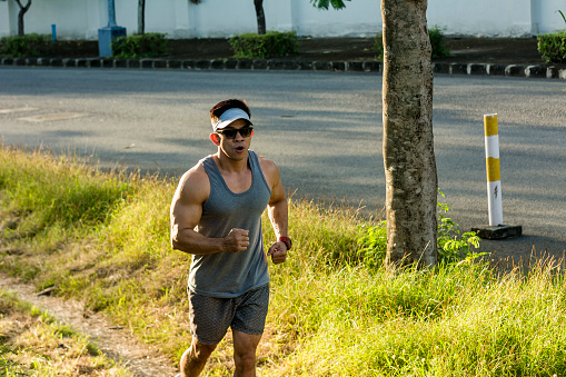 A athletic asian man runs through a pathway near a street doing Fartlek Interval Training. Aerobic exercise and cardio outdoors.