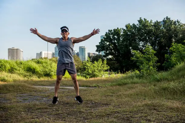 An athletic asian guy does burpees at a open field near the city. Cardiovascular fitness. Working out outdoors.