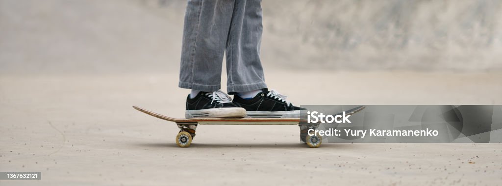 Foot of skateboarder standing on the skateboard on the city street Leisure activity in spring day. Sportive lifestyle. Young man riding skateboard. Photography of feet and skateboard. Closeup photography. Panoramic image Skateboarding Stock Photo