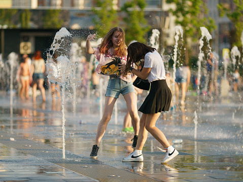 Moscow, Russia - June 21, 2021: People playing with water of fountain. They are having fun and laughing. Hot summer amusement. Lifestyle concept.