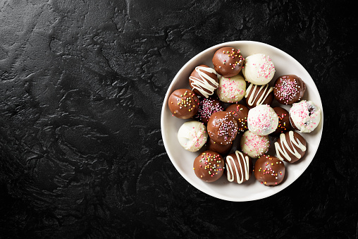 Assorted chocolate truffle candies on black background, top view