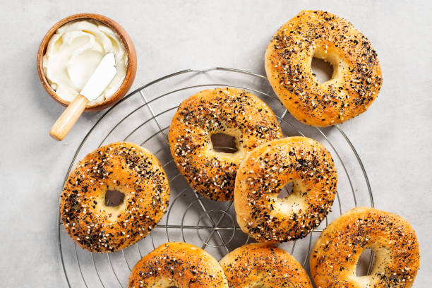 bagels with cream cheese Fresh baked sourdough New York style bagels with cream cheese on light gray table. poppy seed stock pictures, royalty-free photos & images