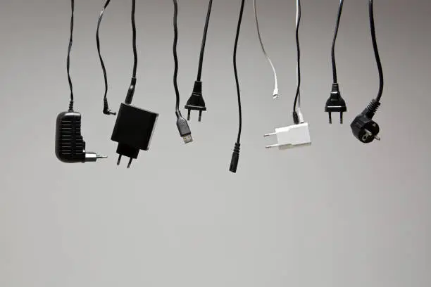 different cables with plugs hang in a row against a neutral background