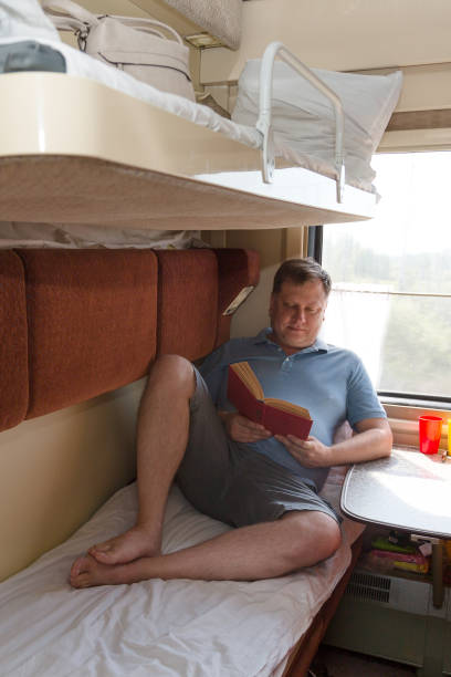 un uomo biondo adulto di 40-45 anni è sdraiato nel suo scompartimento del treno a leggere un libro - 40 45 years immagine foto e immagini stock