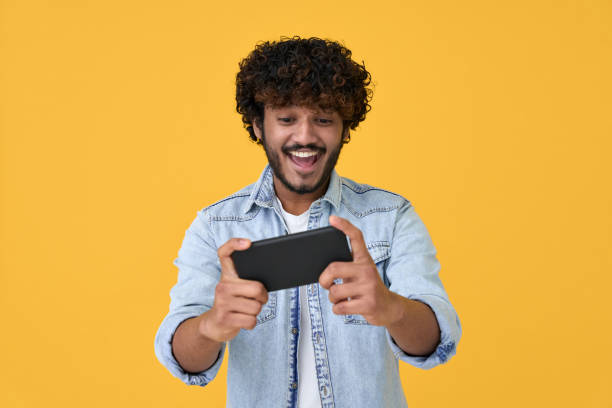 istock Excited young indian man using smartphone playing game on yellow background. 1367646512