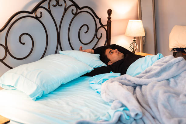 Young man lying down in his bed gazing at the ceiling