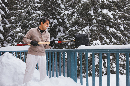 Young man clearing up snow after storm from the balcony