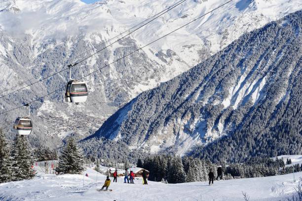 Ski resort view with snowy forest and vintage ski gondolas Ski resort view with snowcapped mountain and skiing people on the slopes under vintage gondolas. courchevel stock pictures, royalty-free photos & images
