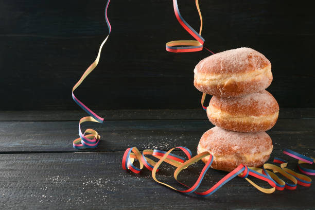 Stacked Berliner doughnuts or Krapfen and some party streamers against a dark rustic background, often served on New Year and carnival, copy space, selected focus stock photo