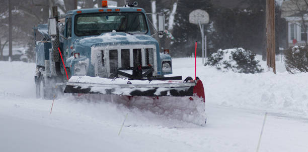 Blue village snowplow clearing a residential street stock photo