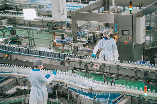 2 Asian Chinese drinking water factory production line workers with PPE examining water bottle working in daily routine 2 Asian Chinese drinking water factory production line workers with PPE examining water bottle working in daily routine food and beverage industry stock pictures, royalty-free photos & images