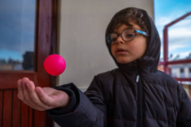 The boy barking the ball in his hand. The ball hangs in the air. Child confident 5 years old with glasses .Ball in focus blur background