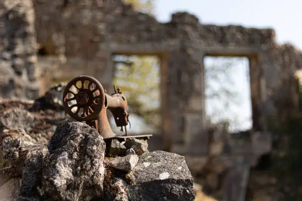 A selective focus of a rusty old sewing machine on ruins in the Martyr village, Oradour-sur-Glane, France