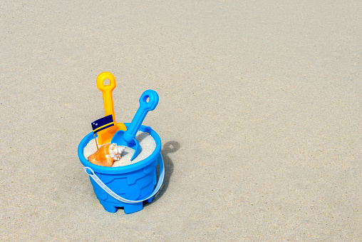 yellow bucket and shovel to make castles on the beach, placed on the sand of the beach on the seashore, in the background the mediterranean sea