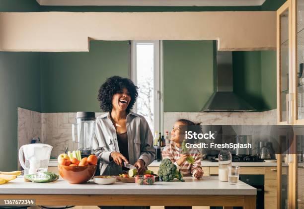 An Africanamerican Single Mother Preparing Vegan Lunch In The Kitchen And Smiling With Her Little Daughter Stock Photo - Download Image Now