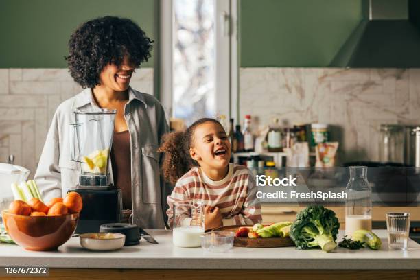 A Beautiful African-American Mother And Her Daughter Standing In The Kitchen And Smiling While Preparing Some Raw Food For Lunch