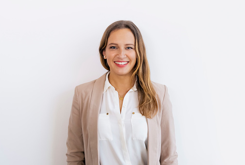 Portrait of happy young woman standing against white wall. Business executive looking at camera and smiling.