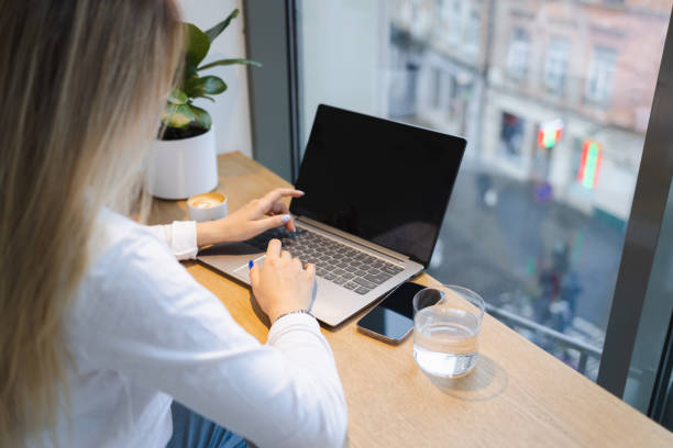 istock Back view of unrecognizable woman working on laptop at table in cafe 1367674720