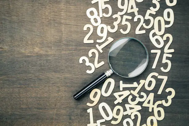 Magnifying glass in scattered numbers on wood background, calculation, mathematics concept