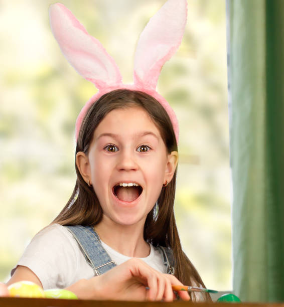 istock Girl in an Easter bunny costume is decorating eggs 1367680538