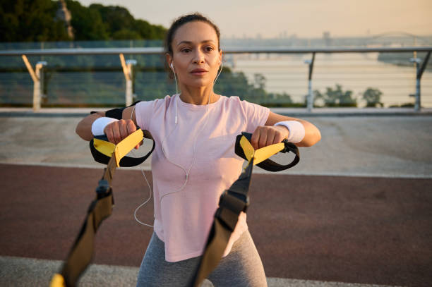 istock Determined female athlete doing bodyweight training with suspension straps against a bridge and river background. Sportswoman exercising outdoor at dawn. Sport, fitness, active lifestyle concept 1367683908
