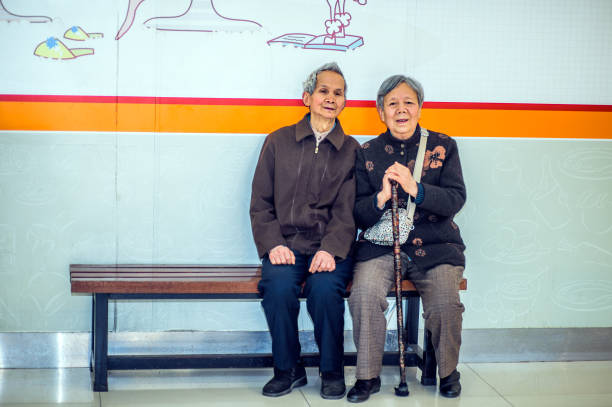 Senior Man and Woman Relaxing on Bench. A  senior couple, 80 years old, is sitting on a bench inside a store, relaxing. Woman holding a walking stick\