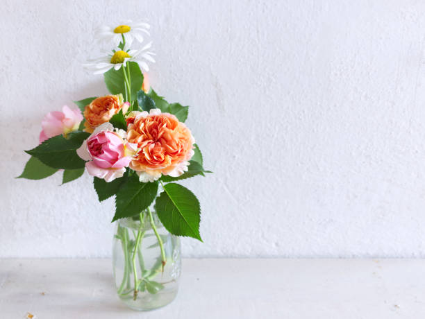 fleurs printanières dans un vase en verre sur une table en bois. arrière-plan de cuisine flou. bouquet de roses et leucanthème. intérieur scandinave élégant et contemporain. - small bouquet photos et images de collection