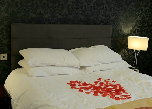 A heart made of red paper petals on a hotel bed
